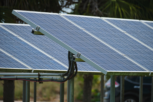 Solar panels installed on stand frame near parking lot for effective generation of clean electricity. Photovoltaic technology integrated in urban infrastructure for electric car charging.