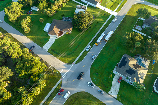 Aerial view of american yellow school bus picking up children at sidewalk bus stop for their lessongs in early morning. Public transportation in the USA.