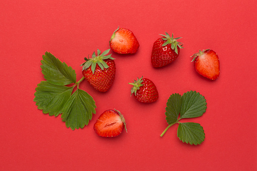 Strawberries with leaves on color background, top view