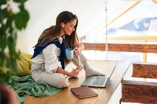 A young woman sits on the floor at home with a laptop, coffee mug in hand, engrossed in her work.