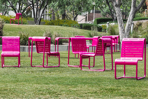 Modern metal pink-colored chairs on a green lawn in city park, comfortable for relaxing in an urban environment.