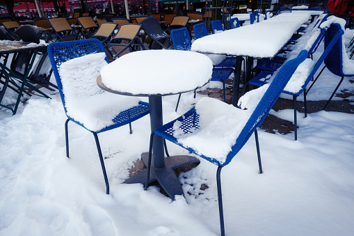 lots of snow on tables and blue chairs at tourist outdoor gastronomy in cologne's old town winter 2024