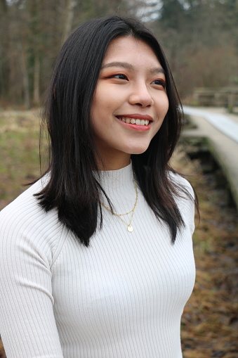 A closeup of a Taiwanese woman with a big smile. She is wearing medium length, black, straight hair, makeup, a necklace, and a white dress.