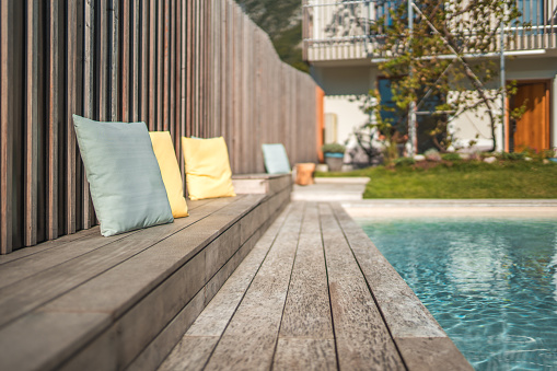 An elegant outdoor setting at a luxury villa showcases a relaxing poolside area with comfortable pillows placed on a wooden deck, inviting a serene vacation atmosphere.