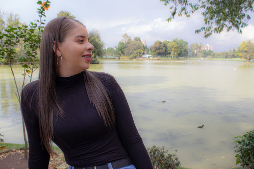 beautiful young woman looking away in a public park in front a lake