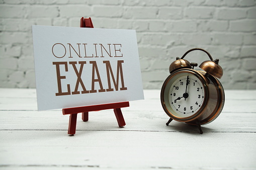 Online Exam text and alarm clock on white brick wall and wooden background