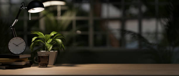 istock An office desk in a modern, dark office at night illuminated by a dim light from a table lamp. 1986508355