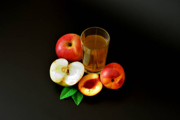 a glass of peach juice with an apple on a black background, next to pieces of ripe fruit. - nectarine fruit full length cross section ストックフォトと画像