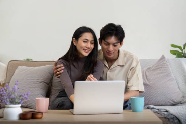 istock Young couple asian using laptop together while sitting on sofa at home 1986565386