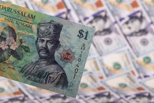 1 Brunei dollar bill against the background of 100 US dollar bills