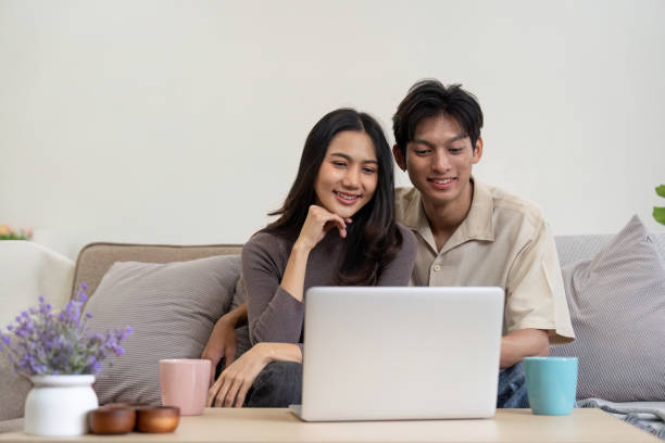istock Young couple asian using laptop together while sitting on sofa at home 1986575760