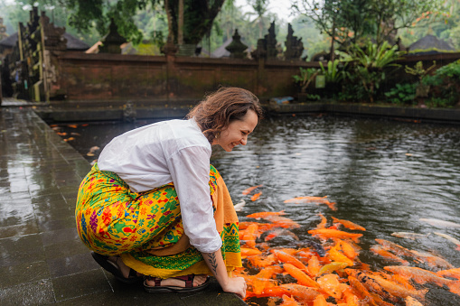 Cheerful woman feeding koi fishes in the pond