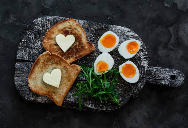 istock Delicious simple breakfast - boiled eggs with soft yolk, arugula, toast with butter on a rustic cutting board on a dark background 1986738062