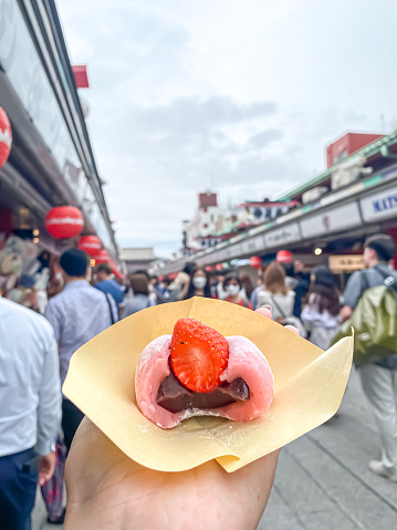 Someone hand holding tasty fancy Ichigo Daifuku that containing strawberry, sweet filling, anko, inside a small round mochi. Japanese food or snack for tourist in Asakusa, Tokyo, Japan.