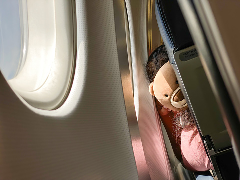 Sad lonely bear doll looking through window aircraft during flight in wing. The view from the airplane window. Daylight Sunny Bright during the day. Concept for solo trip and homesick.