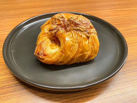 A croissant filled with meat and cheese on black ceramic plate. Concept for breakfast, restaurant and eatery.