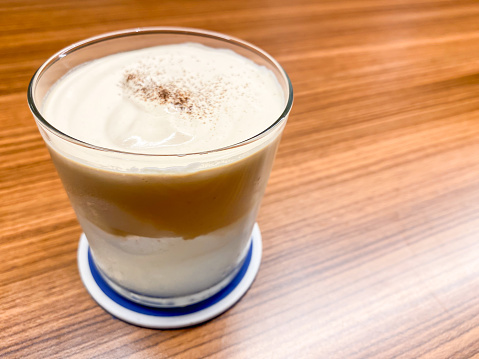 Hot Cappuccino Coffee in a transparent glass on a wooden table.  Caffe Latte or Coffee Milk Drinks in a mug. Concept for working, task, job, business plan. Empty blank copy text space.