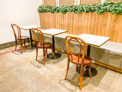 Cafe tables and chairs set made of solid wood against a bright wooden wall background with hanging lamp and ivy plants decoration. Natural interior design concept for cafe, lounge, dining room or living room.
