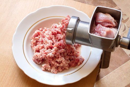 Preparation of minced meat with a manual meat grinder. Meat grinder and fresh minced meat in a plate.