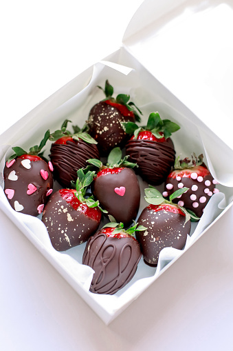 A white box with fresh strawberries dipped in chocolate, decorated with hearts