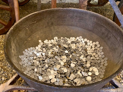 An old cast iron cauldron filled with various coins was previously used for cooking over a fire.