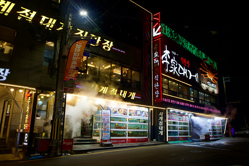 Yeongdeok County, South Korea - December 28, 2023: Outside a three-story snow crab restaurant in Ganggu Port, steam from snow crab cookers fills the air, with a snow crab statue emblazoned on the side and tanks in front.