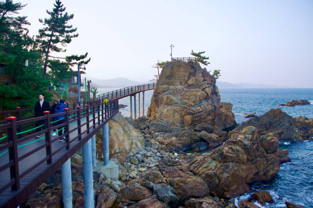 Samcheok City, South Korea - December 28, 2023: A view along the Chogok Yonggul Cave Hiking Trail, with a walking deck in the foreground, a tall rock observatory in the midground, and the East Sea in the background.