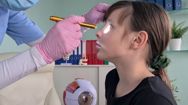 An ophthalmologist carefully examines a young girls eyes with a flashlight, checking for abnormalities