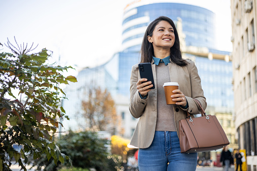 Smiling businesswoman using mobile phone while on the move through the city