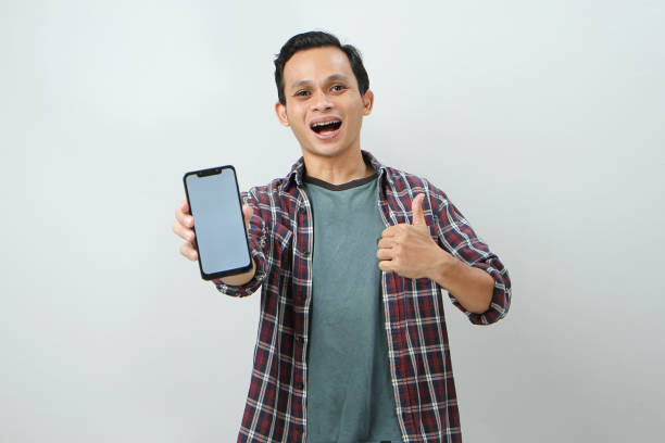 istock Happy asian man holding smartphone and showing blank screen on isolated background 1986977672