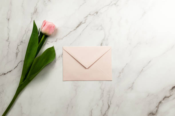 istock Top view of pink tulip and envelope on white marble background. 1987007542
