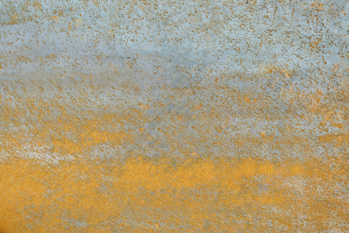 Torn rusty metallic surface with chipping paint over wooden background