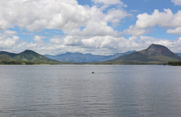 View from Moogerah Dam, across the water, to mountains on the horizon. Semi-overcast day, cumulus clouds hovering over the grey lake. People in the distance are out on a jet-ski, and in boats.
