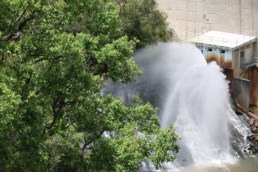 A regular controlled-release fountains out from a station set in the Moogerah Dam wall, providing water for farms and other areas downstream. Trees lean over the foreground view.