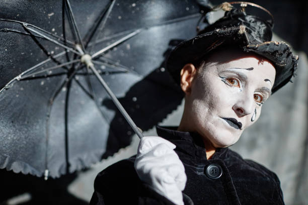Closeup portrait of female mime performer looking at camera on stage and holding umbrella, copy space