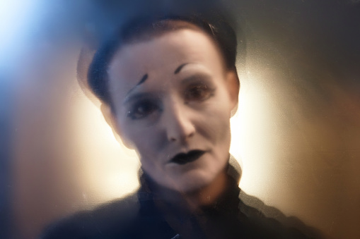 Defocused close up portrait of mime performer looking at camera in stage spotlight, copy space