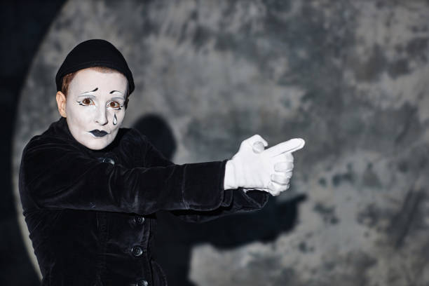 Portrait of mime artist performing on stage in spotlight and looking at camera and shooting pretend gun scene, copy space