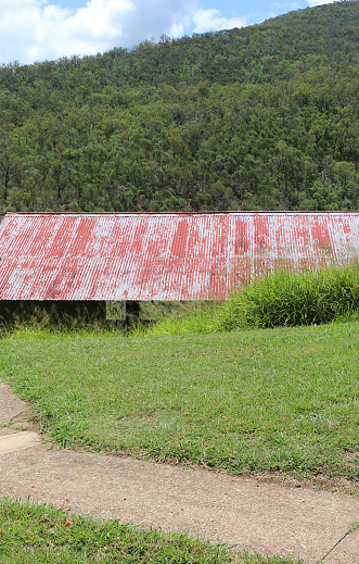 Footpath down to an old meeting shed, hiding between grass area and treed mountainside. Red paint on corrugated roof peeling off. Moogerah Dam, Scenic Rim, South-East Queensland, Australia.