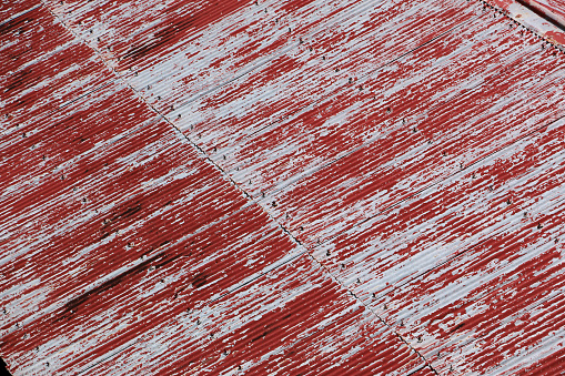 Flaking red paint on old meeting shed roof, wingnuts visible, holding down roof sheets.