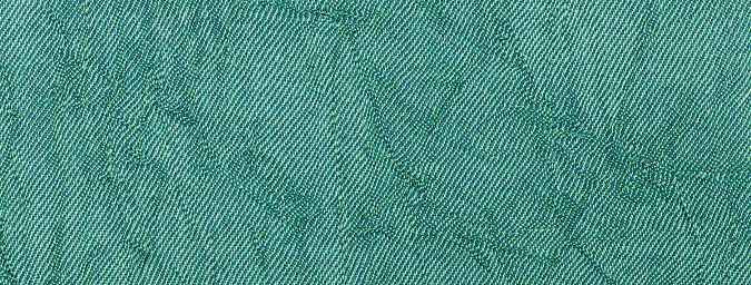 Dark green and cyan wavy background from textile material. Texture of emerald fabric with wrinkled pattern, macro. Upholstery fabric, closeup.