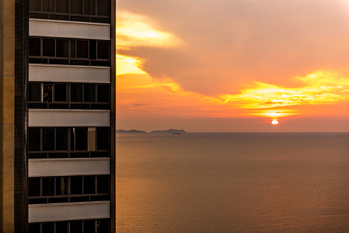 Pattaya, Thailand – April 27, 2019: A scenic view of a sunset over the sea with a high-rise building on the left.