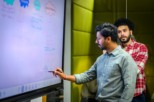 Two young businessmen brainstorming on a interactive whiteboard in a modern office.