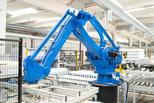 A heavy industrial robotic arm is working as part of a conveyor belt automated factory in a manufacturing plant