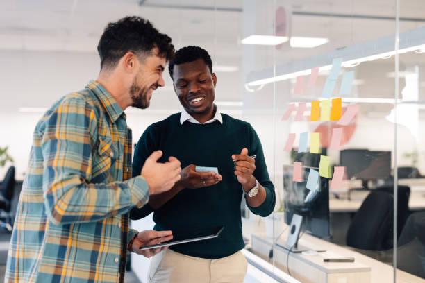 istock Diverse colleagues writing notes on sticky notes on a glass wall in the office 1987106042