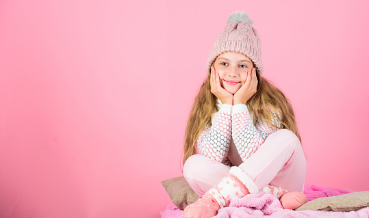 Warm clothes concept. Keep warm and comfortable. Warm accessories that will keep you cozy this winter. Kid girl wear knitted hat relaxing pink background. Child long hair warm woolen hat enjoy warm.