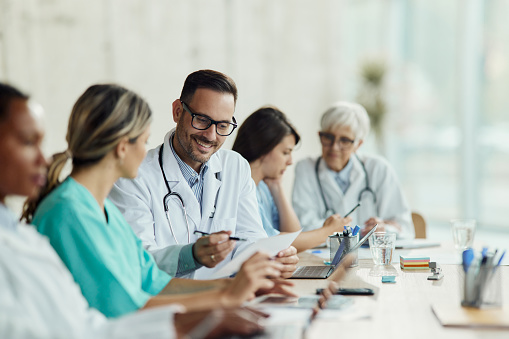 Happy doctor going through medical record with his colleagues during a meeting in hospital.