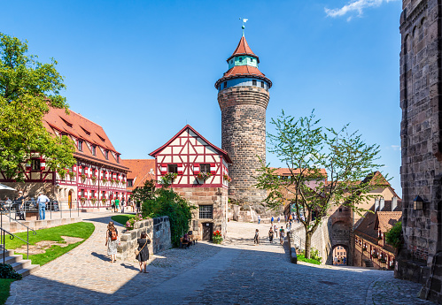 Nuremberg, Germany - August 23, 2023: View of the courtyard of the Kaiserburg, the medieval castle, with the Tiefer Brunnen (well) in the Brunnenhaus half-timbered house and the Sinwellturm (keep).