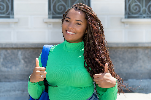 Successful black female student with dreadlocks and green shirt outdoor in the city