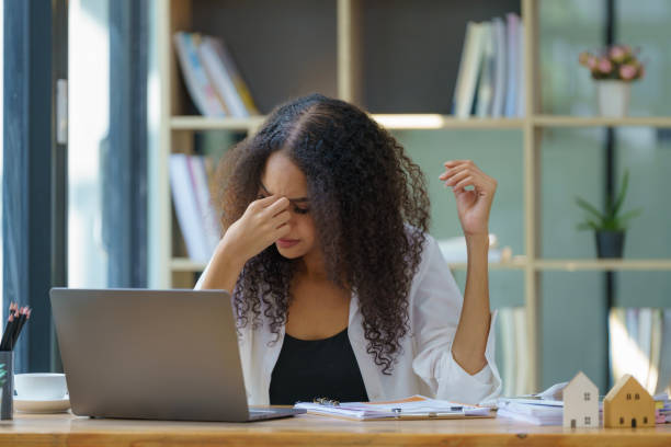 istock Serious black woman entrepreneur using a laptop and reading documents while planning the company's budget and working through financial papers in her office. 1987137405