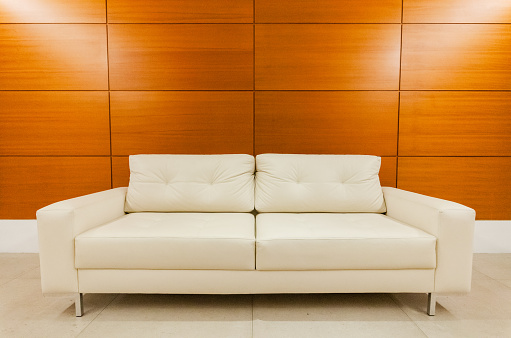 A white leather sofa against a wooden wall in a contemporary interior.